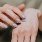 Mgiełki do ciała: czy nawilżają czy tylko pachną i jak je łączyć z balsamem Dłoń kobiety nakładająca nawilżający krem na skórę dłoni