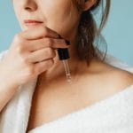 Kobieta w szlafroku nakłada serum na twarz w pielęgnacji cery problematycznej